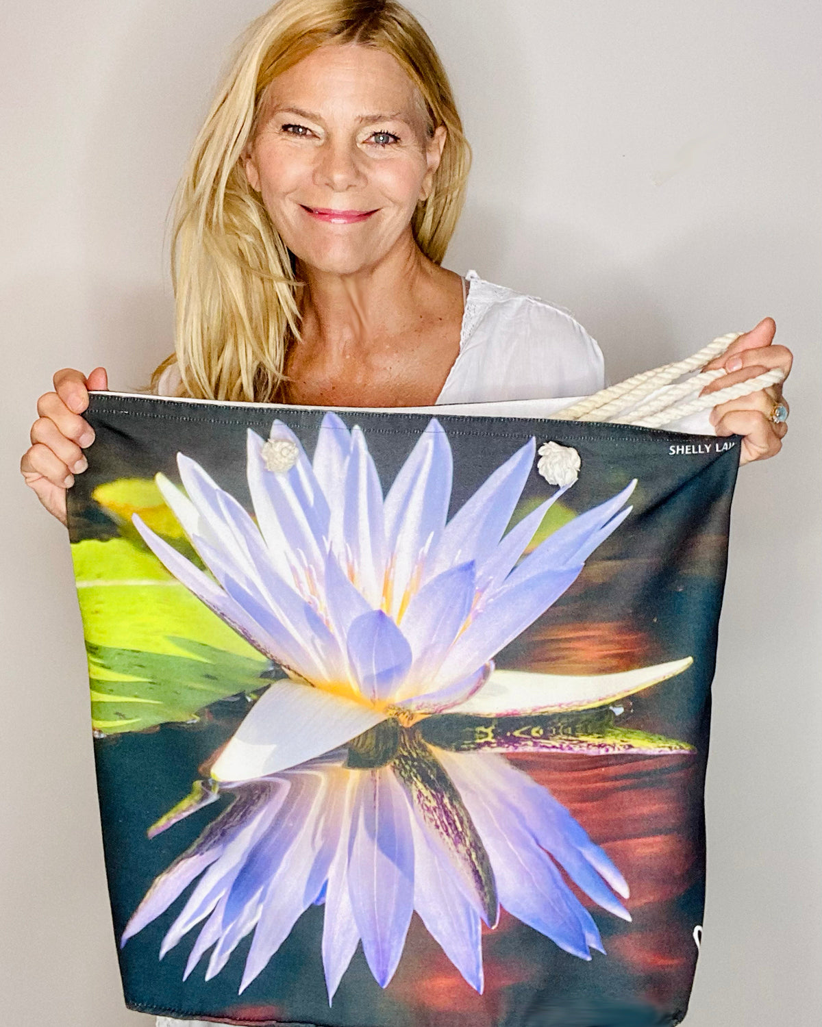 Designer Shelly Lawler holding Lotus tote bag with a water lily design