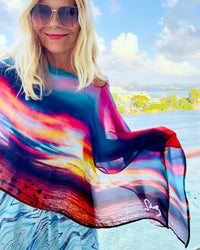 Fire in the Sky Poncho lightweight fabric flowing in wind, vibrant sunset tones, ocean background on cruise ship deck