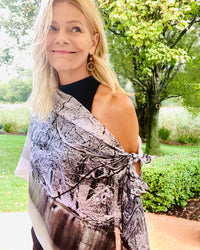 Glass Scarf with signature pre-tied design, black-and-white scarf draped off one shoulder showing winter branch imagery in a garden setting