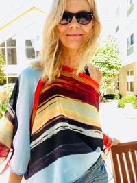 Layercake Poncho styled off one shoulder, highlighting fluid silhouette, lightweight fabric, and signature layered stripe design