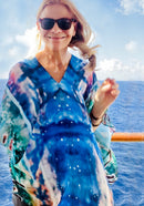 Magic Poncho with slip-over design, worn as a tunic showing original artwork in turquoise with lightweight fabric flowing in the wind against an ocean backdrop
