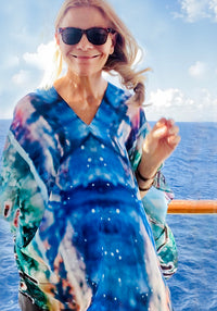 Magic Poncho with slip-over design, worn as a tunic showing original artwork in turquoise with lightweight fabric flowing in the wind against an ocean backdrop
