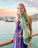 Ombre Poncho styled as a long neckerchief, showing abstract purple and green gradient artwork with lightweight fabric drape against an ocean backdrop
