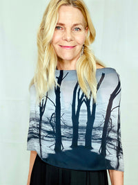 Black-and-white coastal print scarf featuring water and trees draped in a boatneck style with lightweight fluid movement