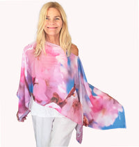Cherry Blossom Poncho with slip-over design, draped over one shoulder showing floral artwork in pinks and white with lightweight fabric flowing in the wind