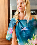 Hummingbird Scarf with signature pre-tied design, worn off one shoulder showing a hummingbird in flight on teal background