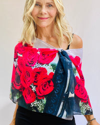 Roses Scarf worn off one shoulder, signature pre-tied design showcasing bold red rose artwork on lightweight flowing fabric