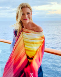 Transatlantic Poncho styled off shoulder, showcasing warm sunset artwork in orange and gold with flowing fabric