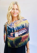 Tuscany Scarf draped across the body, featuring a painterly Italian countryside scene in warm golden tones